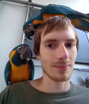 A photo of PhD-student Thibault Boehly surrounded by parrots.