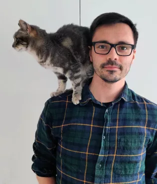 Photo of PhD-student Thomas Rejsenhus Jensen standing with a cat on his shoulder.